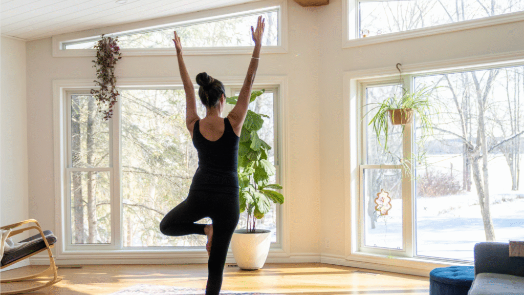 Femme qui pratique le yoga à la maison dans un espace calme et lumineux, symbole d’une pratique douce et sécuritaire pour débuter.