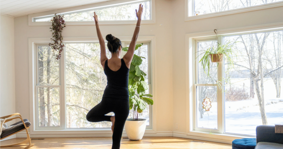 Femme qui pratique le yoga à la maison dans un espace calme et lumineux, symbole d’une pratique douce et sécuritaire pour débuter.