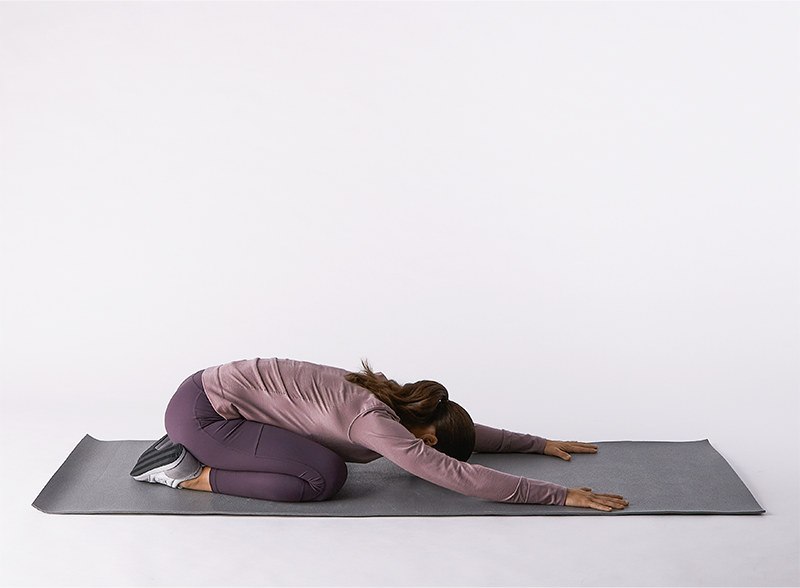 Femme en posture de l’enfant (Balasana) à la maison, relâchant le dos et respirant profondément.
