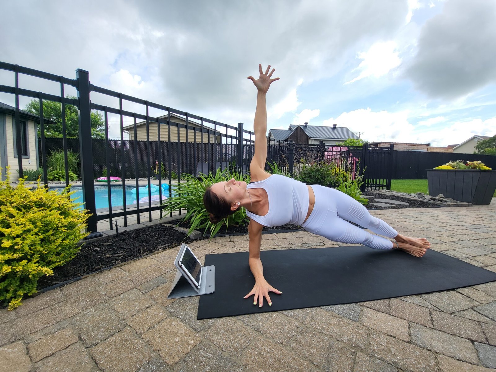 Femme qui pratique le yoga en ligne à l'extérieur, dans une cour joliment aménagée, par une belle journée d'été.